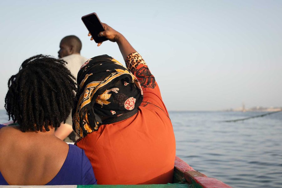 Oumu, vecina de Yaraax, ha intentado cruzar Europa en cayuco y desde su propio barrio y quiere volver a intentarlo. En la imagen, se hace una selfie junto a su hermana, sentadas en un cayuco pesquero de Yaraax. | Sara Aminiyan